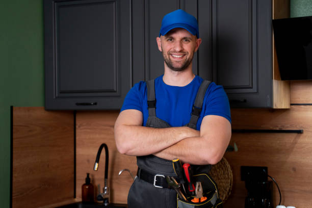 Smiling handsome plumber standing with crossed arms and looking at camera in kitchen stock photo