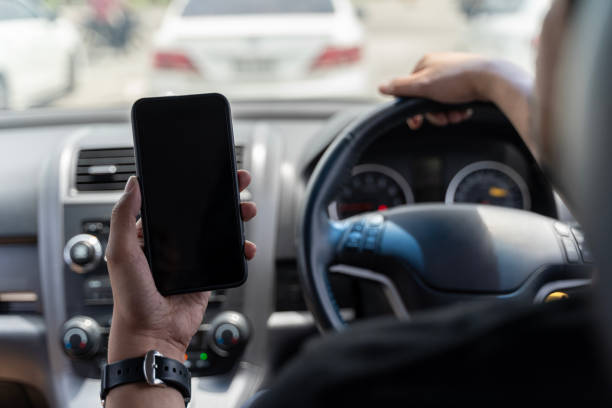 istock Mock up of man using mobile smart phone inside a car. Driver hand holding blank black screen smartphone, searching address. 1679887008