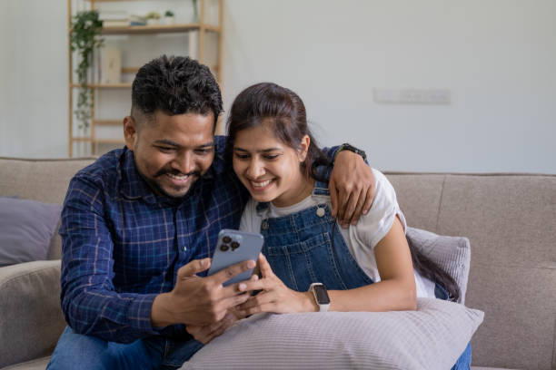 istock Smiling couple embracing while looking at mobile phone, Loving couple relaxing on sofa 1679895598