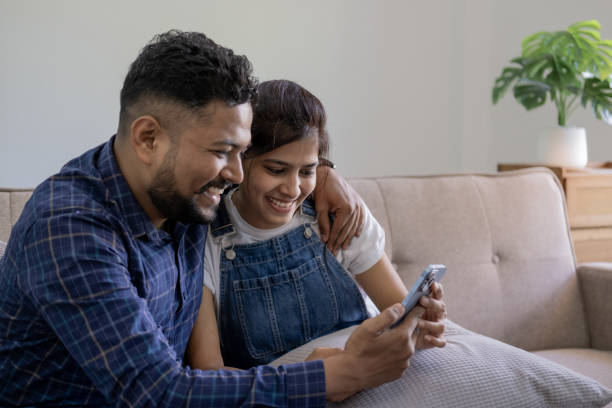 istock Smiling couple embracing while looking at mobile phone, Loving couple relaxing on sofa 1679895603