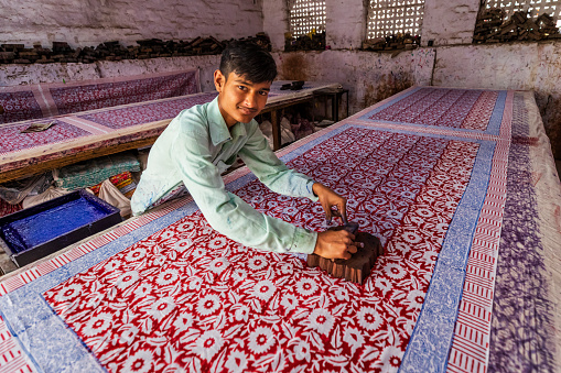 Young man working in block printing factory in Jaipur, India, Jaipur is famous for a screen and block printing. Block printing is the process of printing patterns by means of engraved wooden blocks.