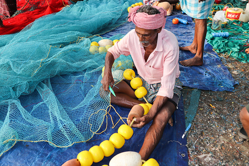 Kochi, Kerala, India-October 6 2022; A Fisherman is seen doing minor repairs on the Nylon nets before embarking on a fishing expedition in Kochi sea in Kerala, India.