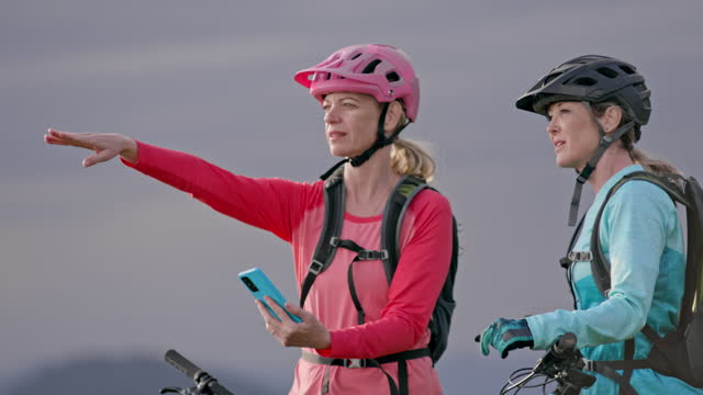 SLO MO LD Two female mountain bikers looking at the smartphone and pointing to the nearby trails