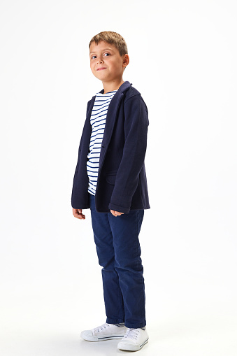 Smiling boy, child wearing blue uniform, smart casual clothes, standing against white studio background. Concept of childhood, school, education, fashion, style. Copy space for ad