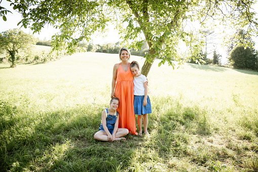 beautiful woman , mother with orange dress with her two daughters outdoor in the nature