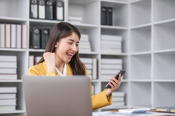 초상화 미소 아름 다운 비즈니스 아시아 디자이너 여자는 전화 컴퓨터를 사용하여 일하는 사무실 책상에 노란색 정장을 입고 있습니다. 중소기업 직원 프리랜서 온라인 중소기업 마케팅 전자 � - conference call flash 뉴스 사진 이미지