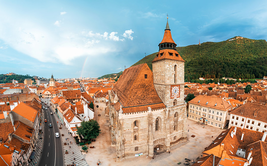 Aerial drone panoramic view of the The Black Church in old Brasov centre, Romania. Old residential buildings around it, narrow streets with moving cars, hills with greenery