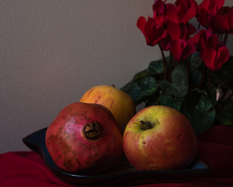 Rosh Hashanah Jewish New Year holiday still life with apples, pomegranate fruit and flowers. Traditional celebration vintage greeting card background.