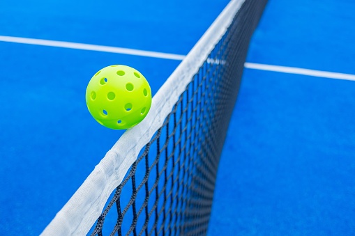 Pickleball ball over the net of a blue court. Concept of new racket sport.