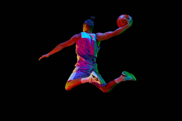 istock Back view image of young guy, basketball player in sportswear training, jumping and throwing ball against black studio background in neon light 1680015607
