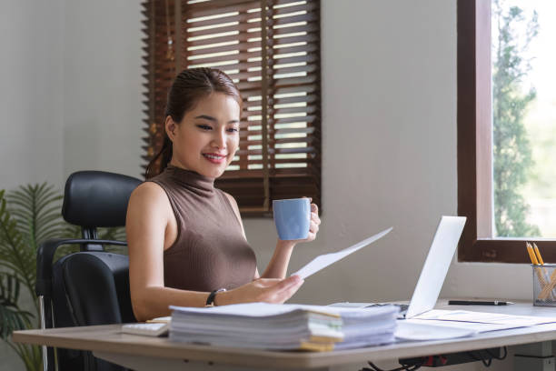 istock Happy Asian businesswoman working and checking work with laptop computer while having a comfortable cup of coffee at office. 1680016204