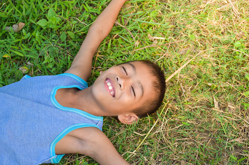 Asian young boy smile cute and charming him lying down on the ground On the background of grass and sunrise  in the morning,top view, close up,child tooth decay.