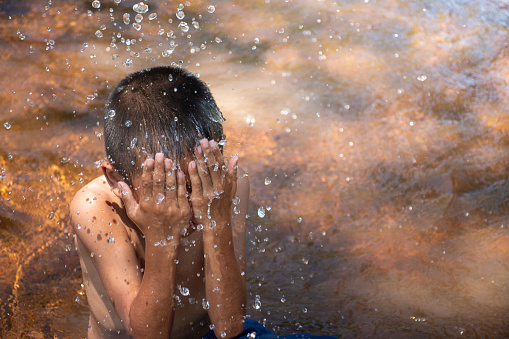 Asian young boy cute and charming playing water in the river on the background of green rice fields and sunrises,child playing water,thai children's lifestyle,happy,fun,joy.