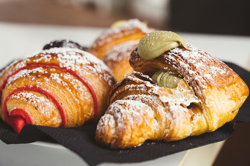 Plate with a variety of fresh croissants with chocolate, pistachio, custar cream stuffing on wooden table indoors, closeup. French pastry.