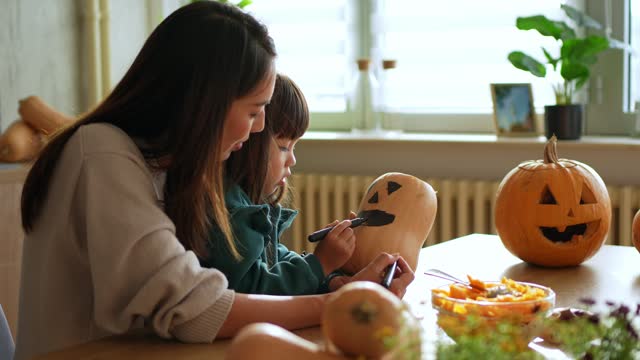 Young Mother And Daughter Creating Outlines On Pumpkins To Carve Them Up For Halloween