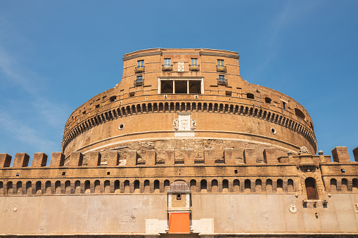 Exterior facade of the ancient towering rotunda of Castel Sant'Angelo or Mausoleum of Hadrian against a blue sky, in the historic old town of central Rome, Italy.