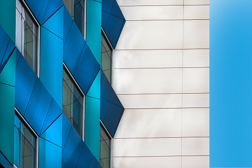 Abstract Office Building Facade featuring windows. There is a right support wall that would be perfect for copy space. You can see blue sky to the right of the image
