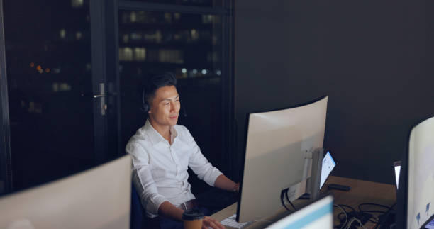 istock Call center, agent and man, crm and contact us, phone call with night work and communication, pc and headset. Telemarketing, customer service or tech support, talk to client and Asian agent help desk 1680095809