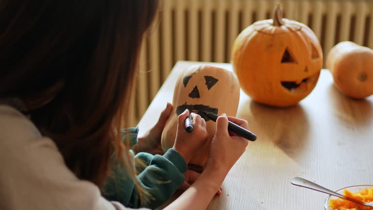 Young Mother And Daughter Creating Outlines On Pumpkins To Carve Them Up For Halloween