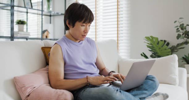 Gen Z queer man non-binary at home. Asia LGBT young guy adult people happy relax sitting at sofa use omni channel easy buy now pay later BNPL shop store. Reading online bank loan news on web page app. gen z hombre queer no binario en casa. asia lgbt joven adulto personas felices relajarse sentado en el sofá usar omnicanal fácil comprar ahora pagar más tarde bnpl tienda tienda. leer noticias de préstamos bancarios en línea en la aplicación de la p�