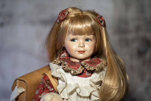 Realistic porcelain antique vintage doll or toy,  blonde hair and vintage dress.