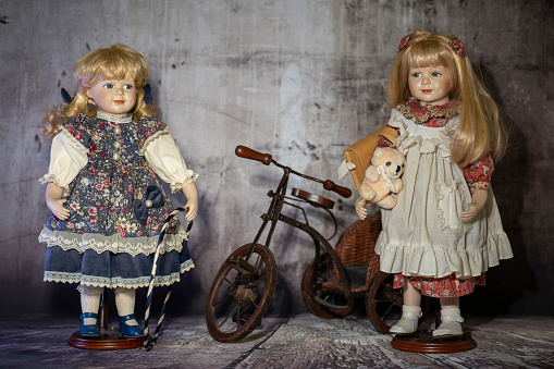 Two Realistic porcelain antique vintage girl doll or toy,  blonde hair and vintage dress with bicycle.