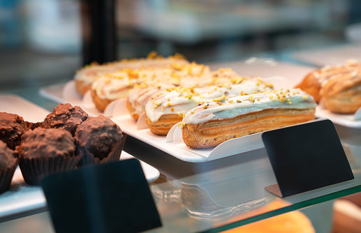 Fresh pistachio eclairs and other desserts in a glass showcase in a cafe or shop. Close-up. Selective focus.
