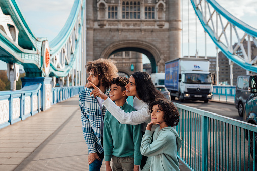 A Multiracial family stand together pointing at landmarks they can see from the bridge