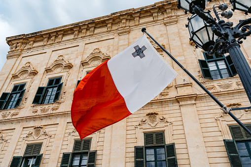 Maltese flag waving in the wind on the street with Aubrage de castille in the background in Malta.