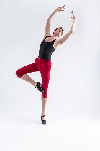 Contemporary Ballet of Flexible Athletic Man Posing in Red Tights in Ballanced Dance Pose With Hands Lifted in Studio on White.Vertical Composition