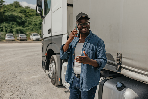 Young black truck driver using mobile ohone in front of the semi-truck