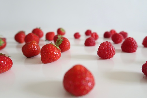 Close-up image of strawberries and redcurrants on a white table, white background, healthy berry mix, sweet snack, no people, fresh berries, vibrant red color, blurry background