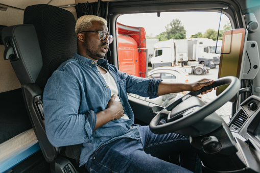 Young black man with having stomach problems while driving semi truck