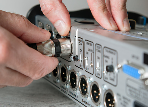 A male hand unplugs a male XLR cable from the input of a mixing console.