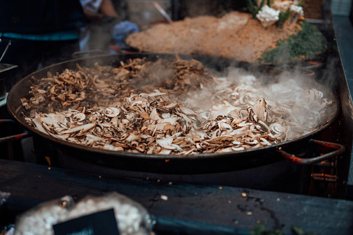 Mushrooms being cooked in a large pan at a street food market