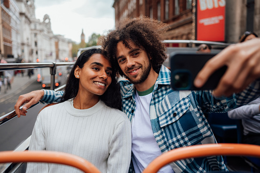 A couple sit at the top of a sightseeing bus taking a selfie.