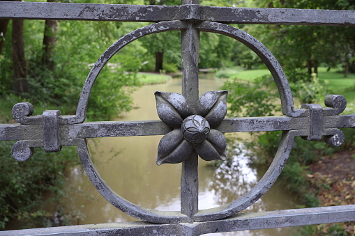 A picture taken of a decoration of one of the metal bridges around the Englisher Garten, with the river and the forest around it visible in the blurred background.