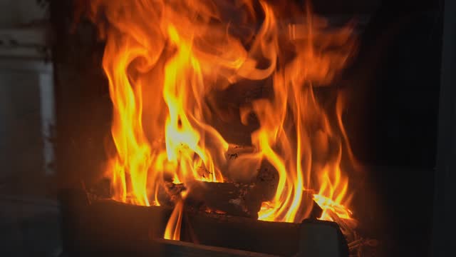 A fire burns in a fireplace to keep warm on a winter evening. Close-up of orange roaring flames in a modern fireplace. Crest of flame on burning wood behind fireproof glass. Video footage in 4K 25FPS.