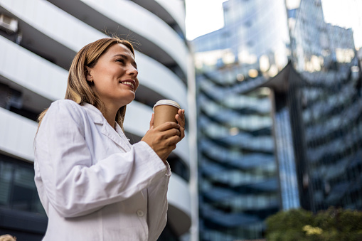 Shot of a young female doctor having a coffee while having break. Young female doctor in white coat on a coffee break.