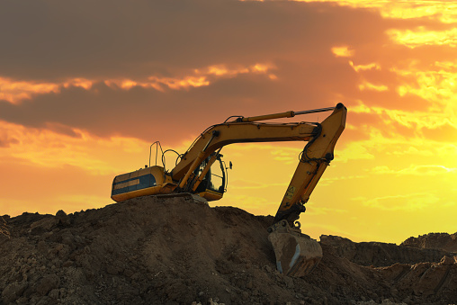Excavator on earthmoving at open pit mining. Backhoe dig sand, gravel in quarry on sunset. Heavy construction equipment on excavation at construction site. Mining excavator on foundation development