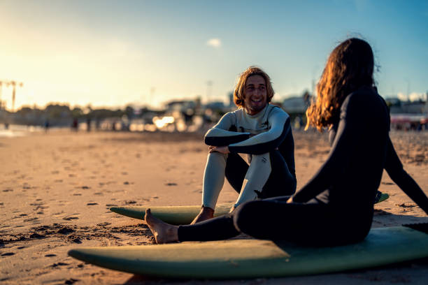 istock Two surfers with surfboard sitting on beach resting after surfing at sunset. 1680289125