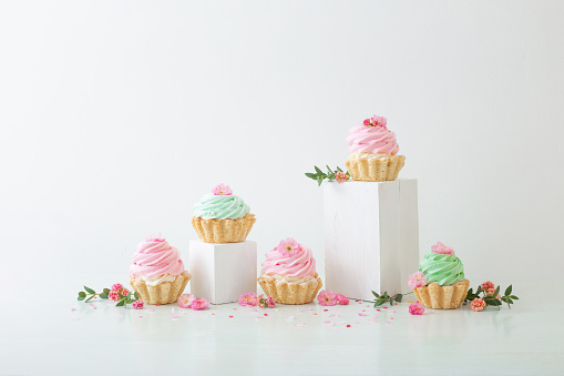 pink and green cupcakes with spring flowers  on wooden podiums on white  background