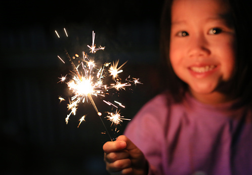 Little Asian child girl enjoy playing firecrackers. Focus at fire sparklers.