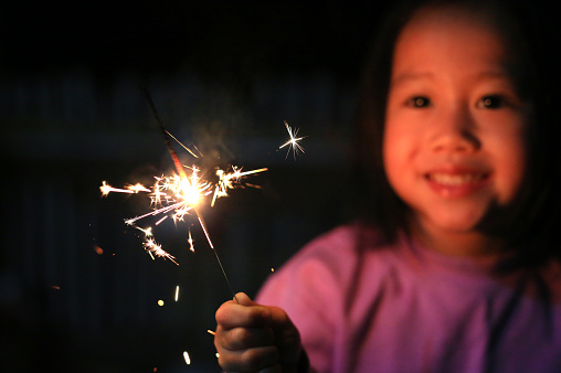 Little Asian girl playing fire sparklers in the dark.