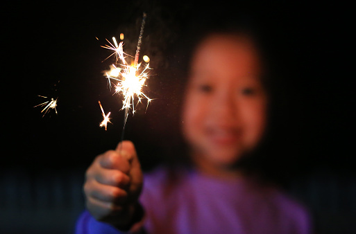 Close up little Asian girl playing fire sparklers in the dark at night.