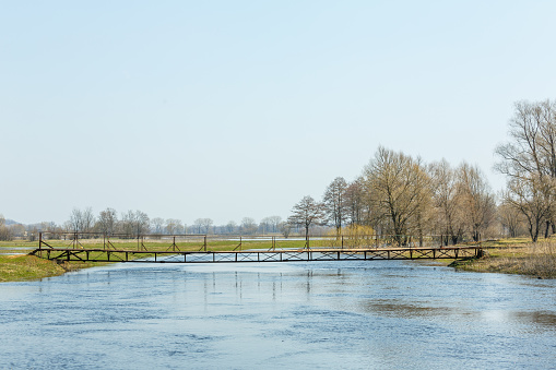River bank in spring. A small pedestrian bridge across the river.