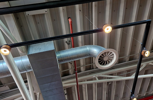 the air handling unit is on the ceiling of the building and is visibly left uncovered. the lights and pipes running under the tin roof give it an industrial feel. whire, circulation, extractor, ductwork, ventilation, ventilated