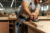Close up of carpenter hands sanding wood with orbital sander at workshop