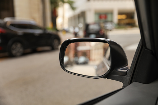 car's rearview mirror, reflecting a scenic road behind. The mirror symbolizes nostalgia, reflection, and the journey of life, capturing moments from the past