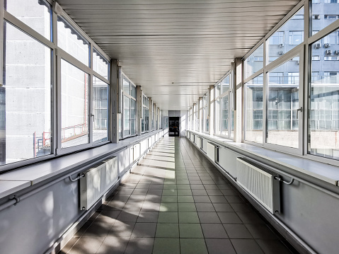 Panoramic view of an empty technical tunnel with glass windows. A corridor structure made of metal and glass illuminated by bright sunlight. Commercial architecture.